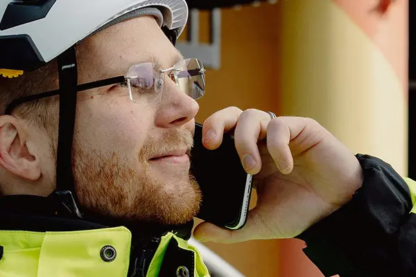 A man in reflective clothing and a white helmet looking to the right and talking on a mobile phone. A man in reflective clothing and a white helmet looking to the right and talking on a mobile phone.